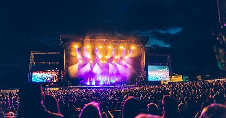 performers on stage during the night time with crowd watching at Hardwick Live Festival